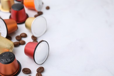 Many coffee capsules and beans on white table, closeup. Space for text