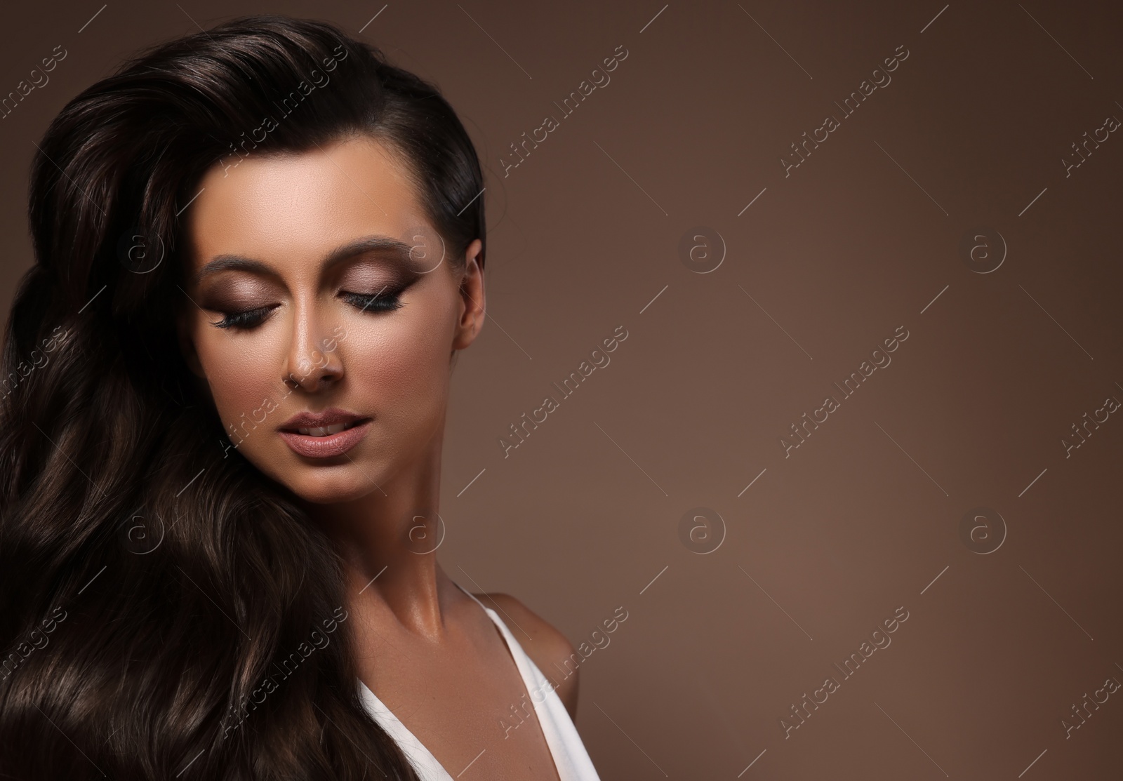 Image of Gorgeous woman with shiny wavy hair on brown background, space for text. Professional hairstyling