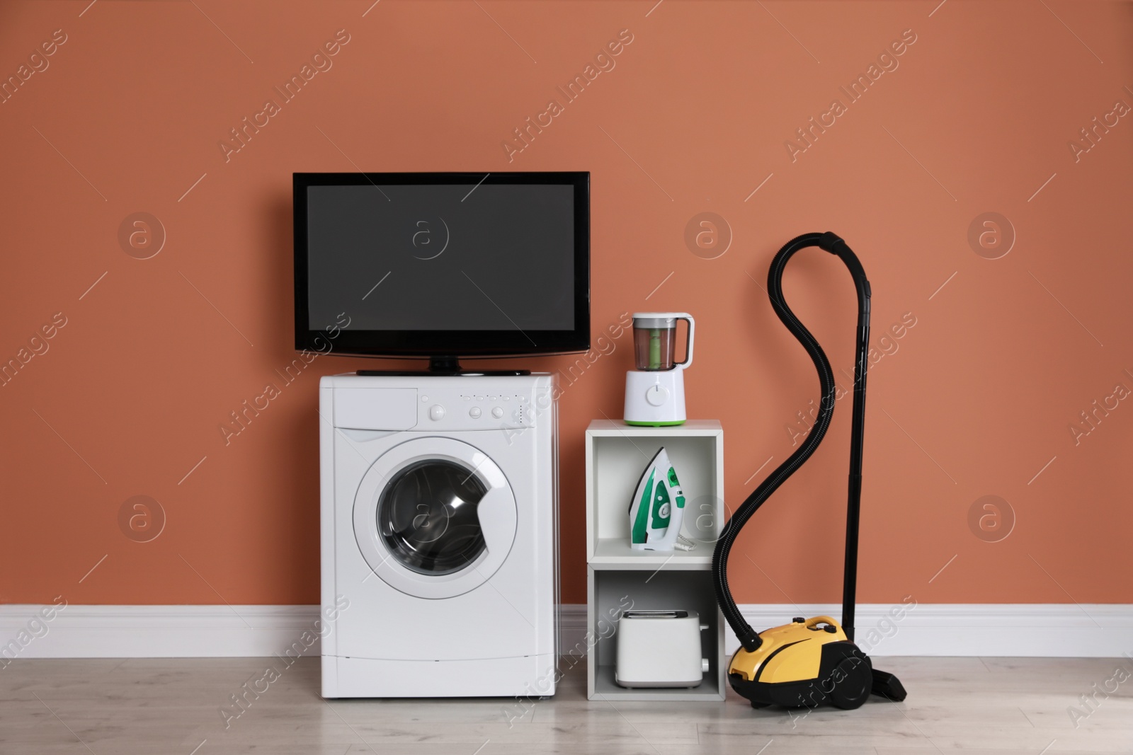 Photo of Set of different home appliances with vacuum cleaner near brown wall indoors