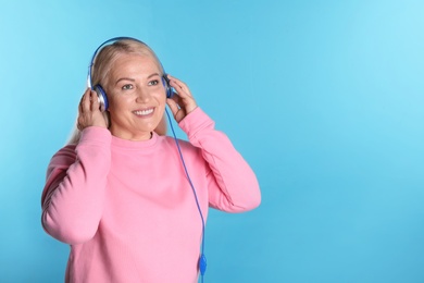 Photo of Mature woman enjoying music in headphones on color background. Space for text