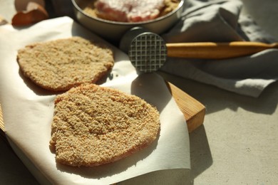 Photo of Cooking schnitzel. Raw pork chops in bread crumbs, meat mallet and ingredients on grey table, closeup