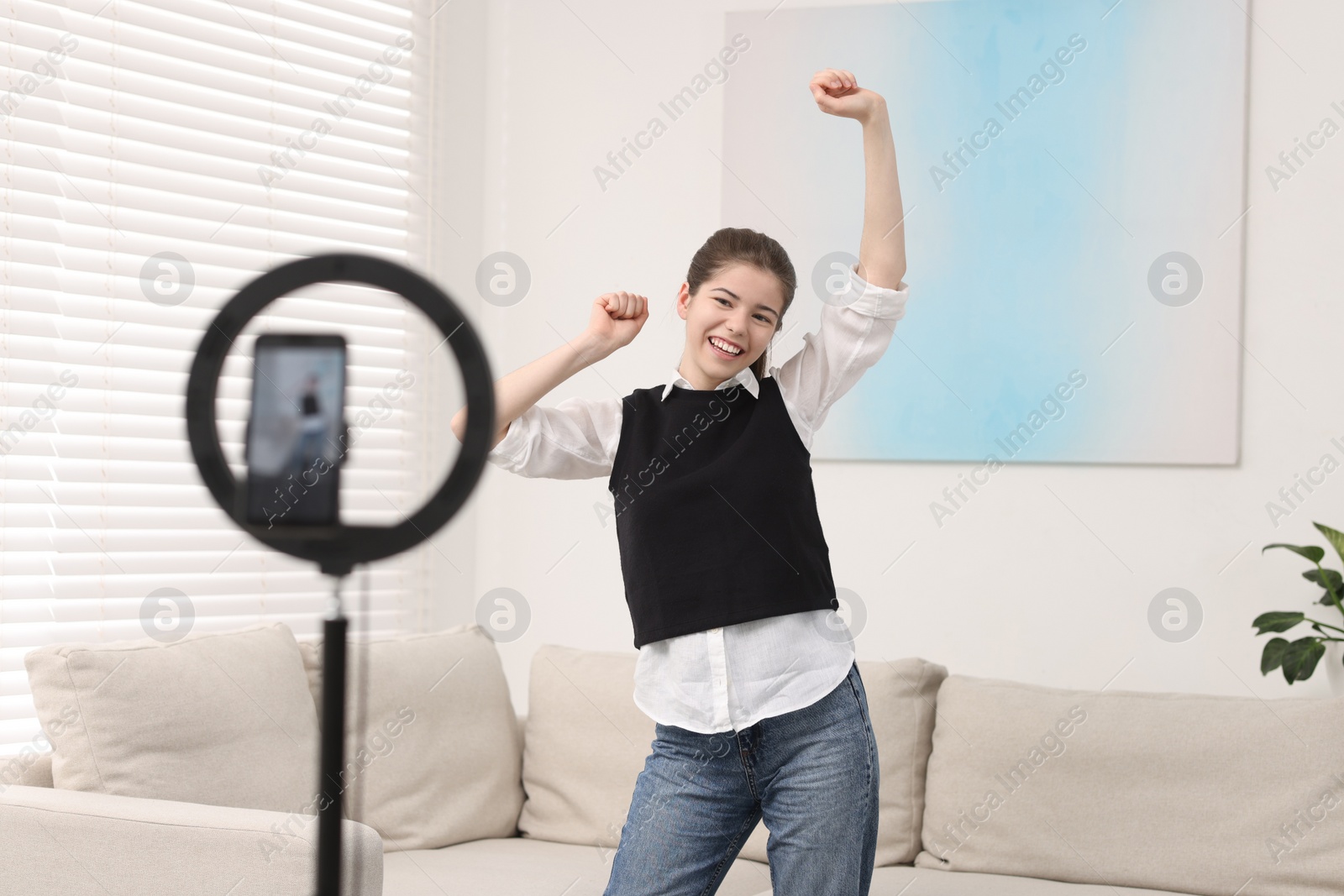 Photo of Smiling teenage blogger dancing while streaming at home