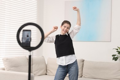 Photo of Smiling teenage blogger dancing while streaming at home