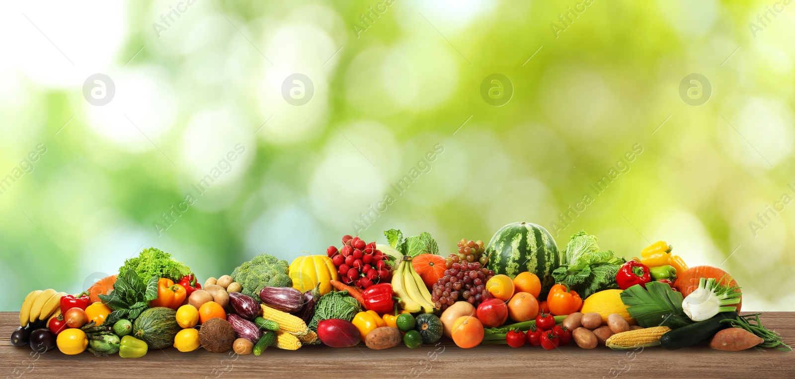 Image of Assortment of fresh organic vegetables and fruits on wooden table against blurred green background. Banner design 