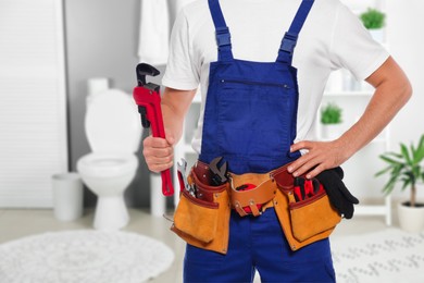 Image of Plumber with pipe wrench and tool belt in bathroom, closeup. Space for text