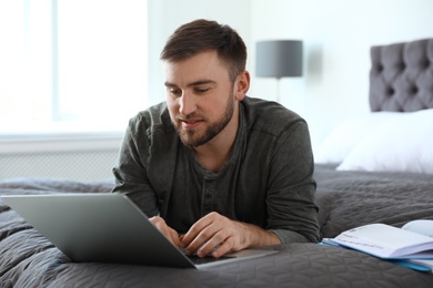 Young man using laptop while lying on bed at home