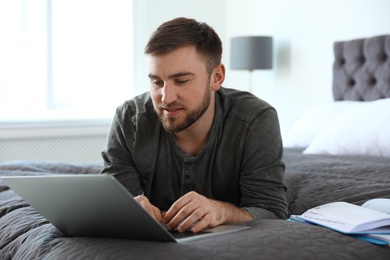 Photo of Young man using laptop while lying on bed at home