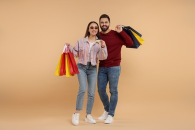 Happy couple with shopping bags showing credit card on beige background