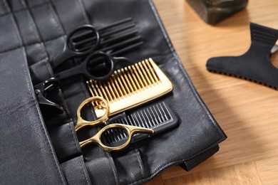 Hairdresser tools. Professional scissors and combs in leather organizer on wooden table, closeup