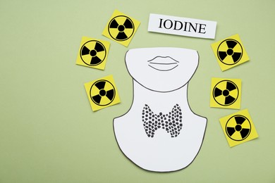 Photo of Paper note with word Iodine, radiation signs and cutout of thyroid gland on olive background, flat lay. Space for text