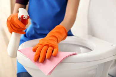 Photo of Woman cleaning toilet bowl in bathroom, closeup