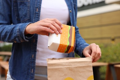 Photo of Lviv, Ukraine - October 9, 2023: Woman putting burger in paper bag outdoors, closeup