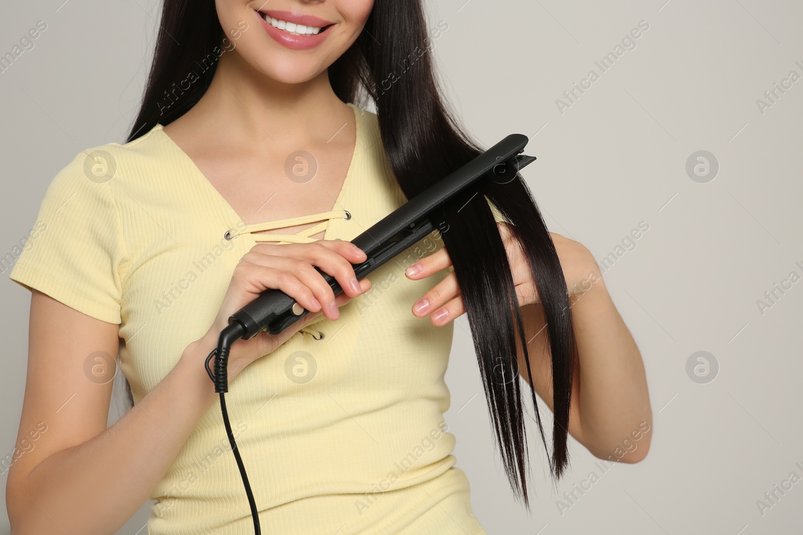Photo of Happy woman using hair iron on light grey background, closeup