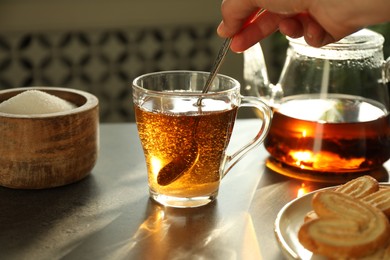 Photo of Woman stirring tea with spoon at dark table, closeup