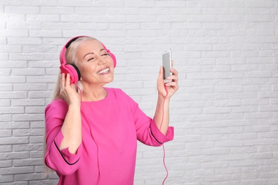 Photo of Mature woman in headphones with mobile device against brick wall. Space for text