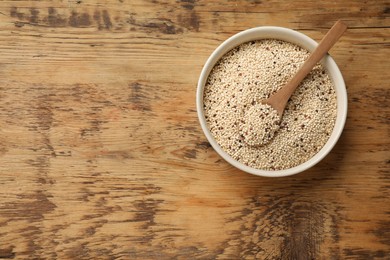 Raw quinoa seeds and spoon in bowl on wooden table, top view. Space for text