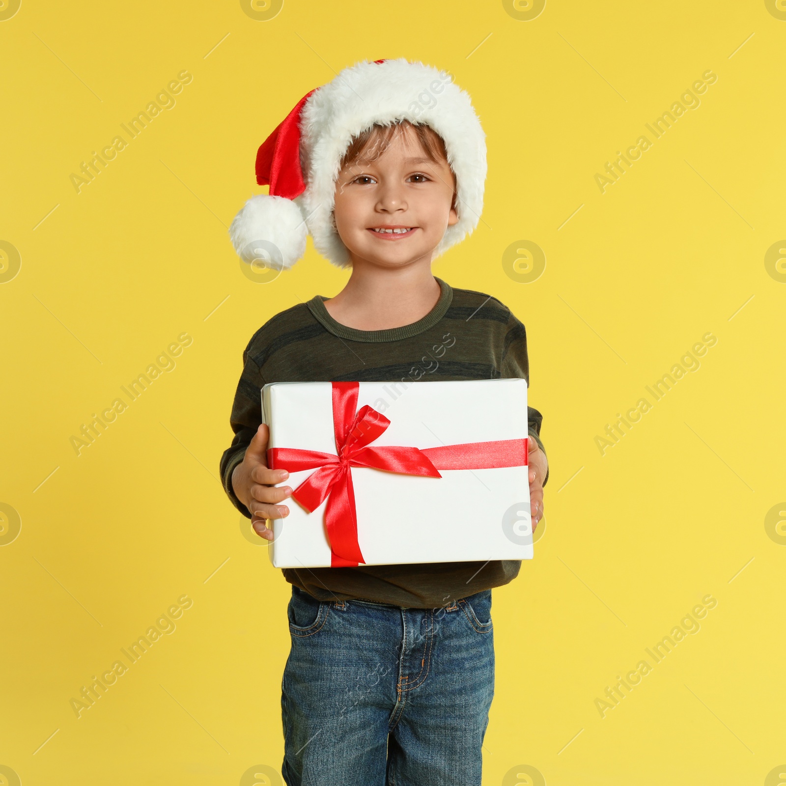 Photo of Cute little boy in Santa hat with Christmas gift on yellow background