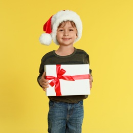 Photo of Cute little boy in Santa hat with Christmas gift on yellow background