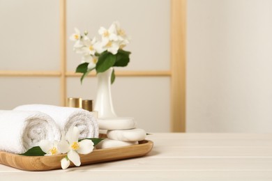 Photo of Beautiful jasmine flowers, towels and spa stones on white wooden table, space for text