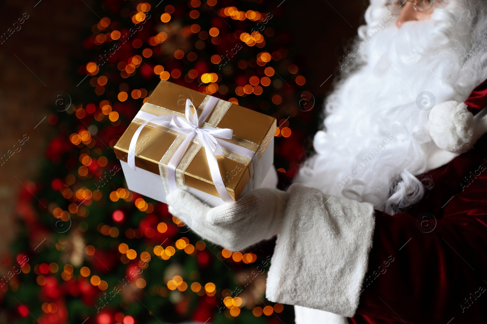 Photo of Santa Claus holding Christmas gift against blurred festive lights, closeup