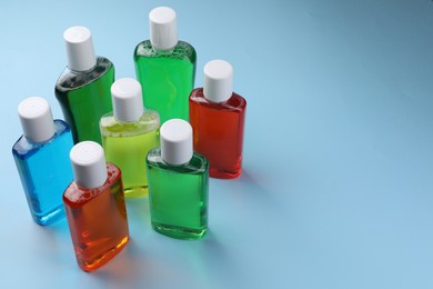 Photo of Fresh mouthwashes in bottles on light blue background. Space for text
