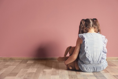 Little girl with toy sitting on floor near color wall in empty room. Autism concept