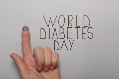 Photo of Woman showing finger with drawn blue circle near text World Diabetes Day on light background, closeup