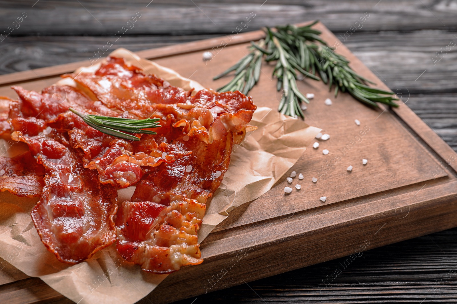 Photo of Board with fried bacon on wooden background