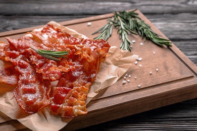 Photo of Board with fried bacon on wooden background