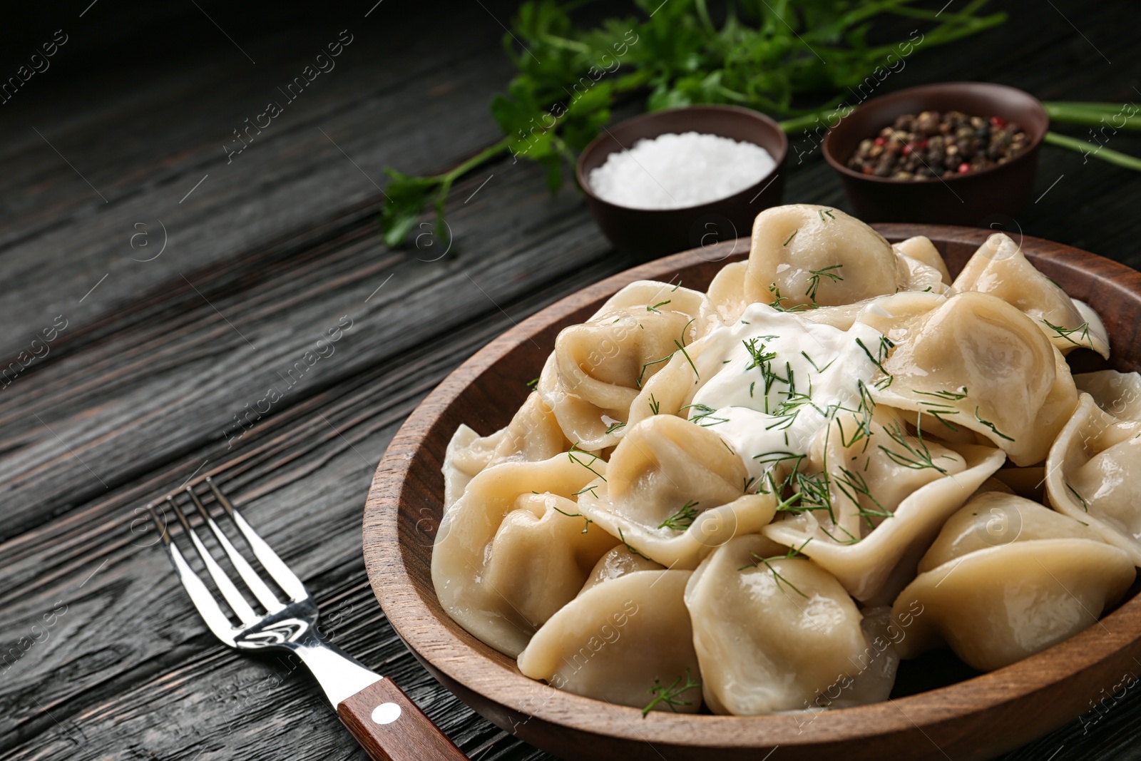 Photo of Tasty dumplings with sour cream in bowl on black wooden table, closeup