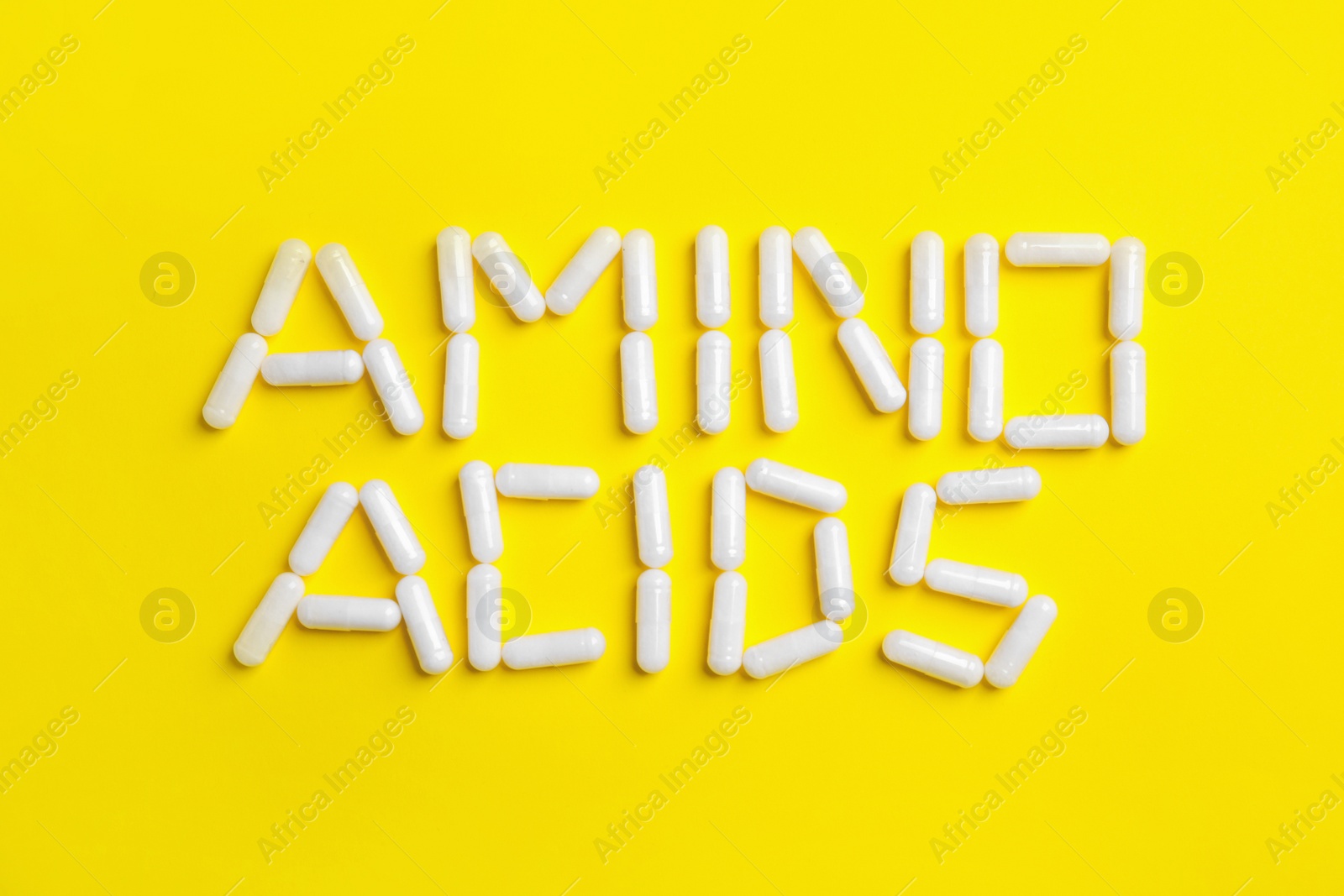 Photo of Phrase Amino acids made of pills on yellow background, flat lay