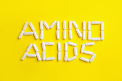 Photo of Phrase Amino acids made of pills on yellow background, flat lay