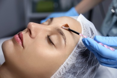 Cosmetologist applying chemical peel product on client's face in salon, closeup