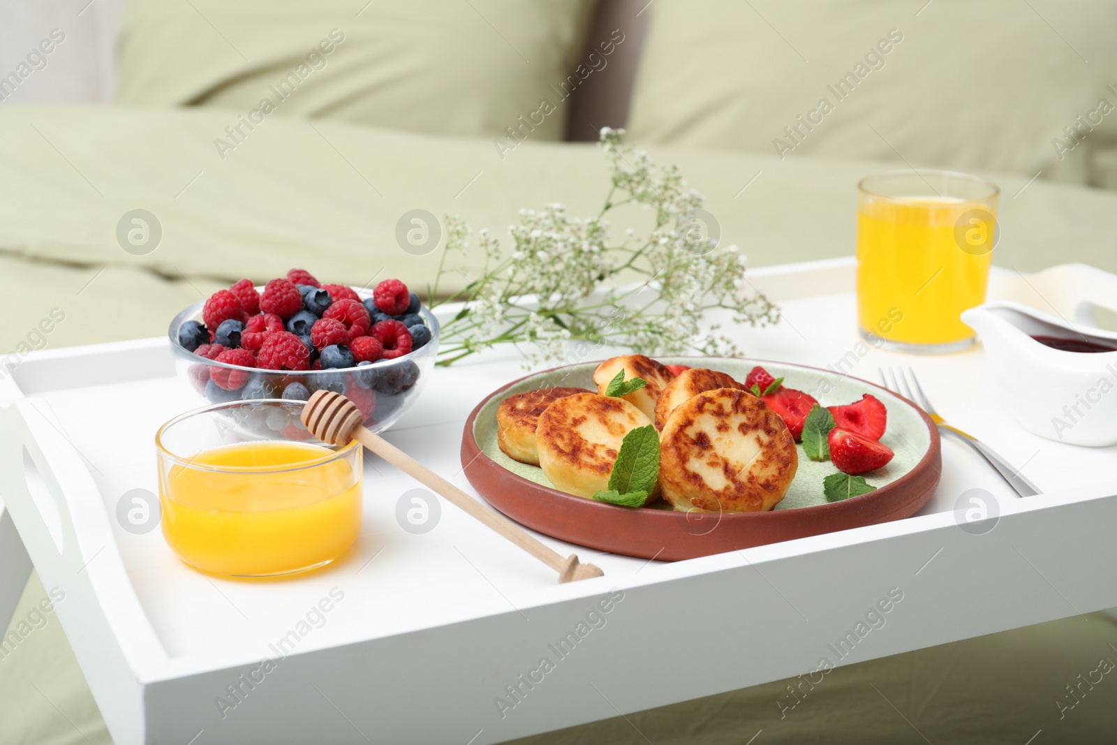 Photo of Tasty breakfast served in bedroom. Cottage cheese pancakes with fresh berries and mint on white tray