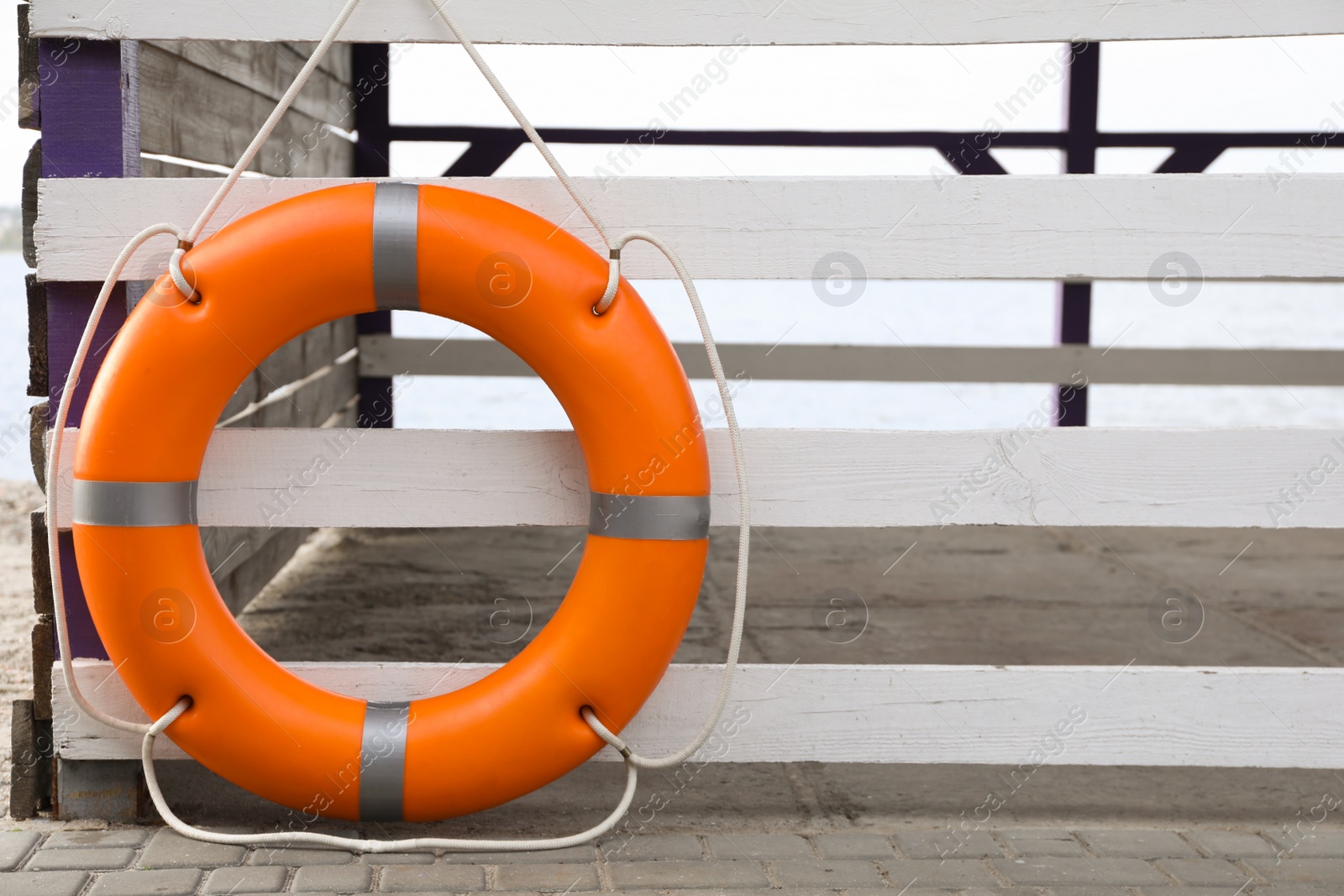 Photo of Orange life buoy hanging on white wooden fence at beach, space for text