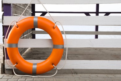 Photo of Orange life buoy hanging on white wooden fence at beach, space for text