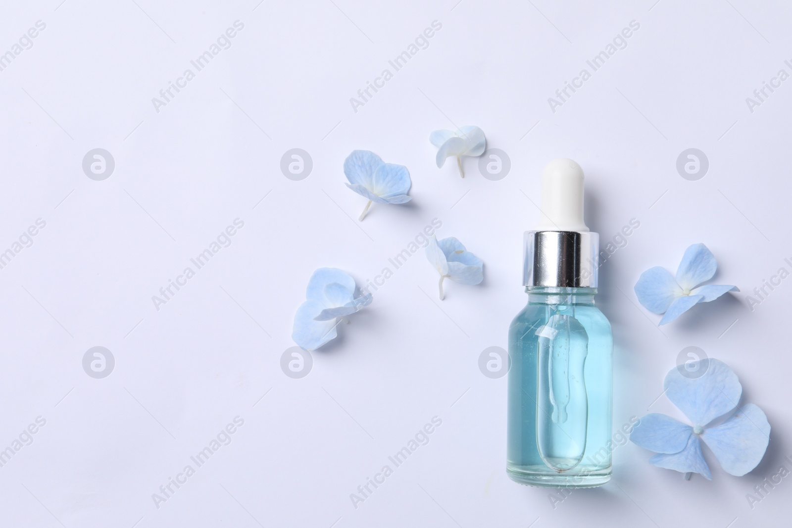 Photo of Bottle of cosmetic serum and beautiful flowers on white background, flat lay. Space for text