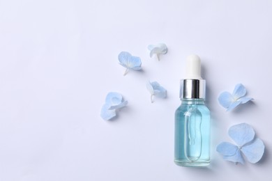 Photo of Bottlecosmetic serum and beautiful flowers on white background, flat lay. Space for text