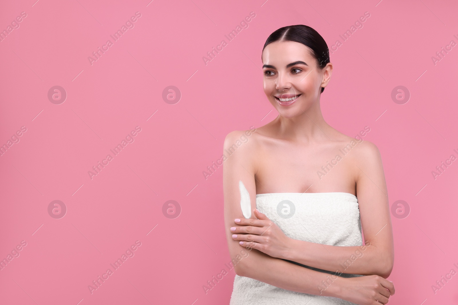 Photo of Beautiful woman with smear of body cream on her arm against pink background, space for text