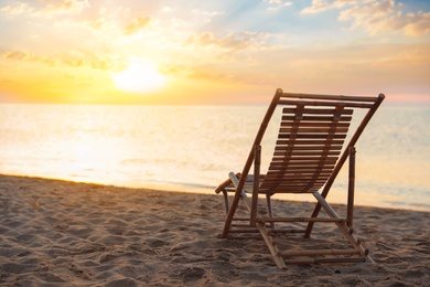 Photo of Wooden deck chair on sandy beach at sunset. Summer vacation