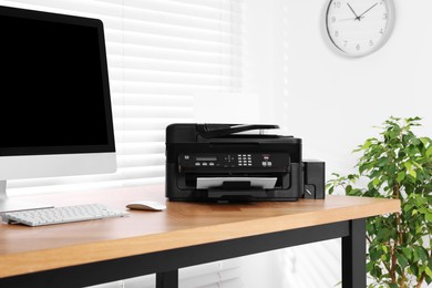 Modern printer with paper near computer on wooden table in home office