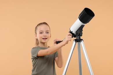 Photo of Cute little girl with telescope on beige background