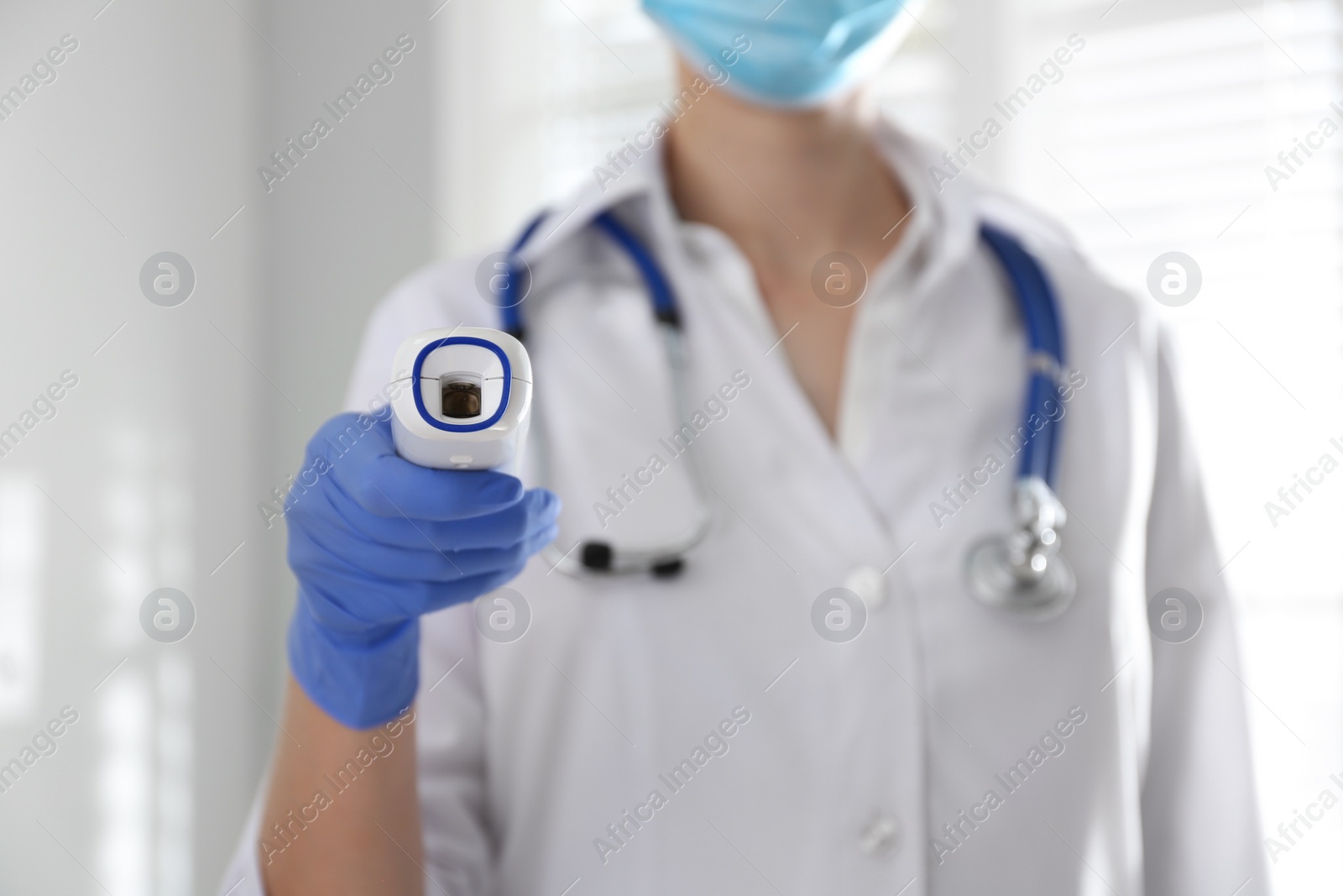 Photo of Doctor holding non contact infrared thermometer indoors, focus on hand. Measuring temperature