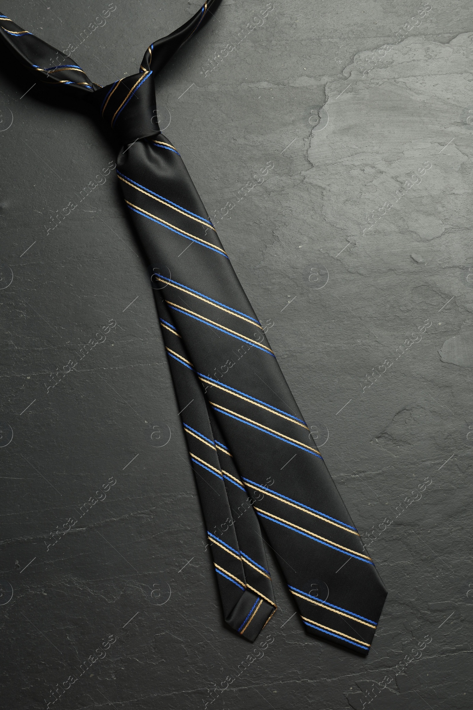 Photo of One striped necktie on grey textured table, top view