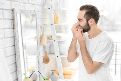 Young man flossing his teeth in bathroom