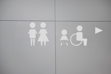 Image of White public toilet sign with arrow showing direction on wall