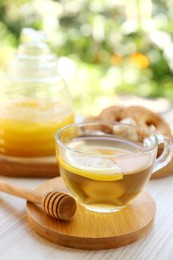 Cup of delicious tea with lemon and honey on white wooden table outdoors