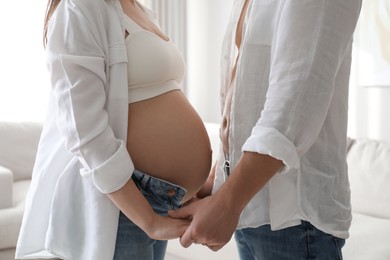Photo of Pregnant young woman with big belly and her husband holding hands together at home, closeup