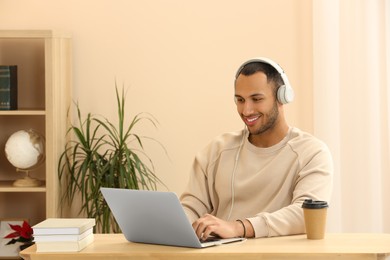 Photo of Smiling African American man in headphones working on laptop at wooden table indoors