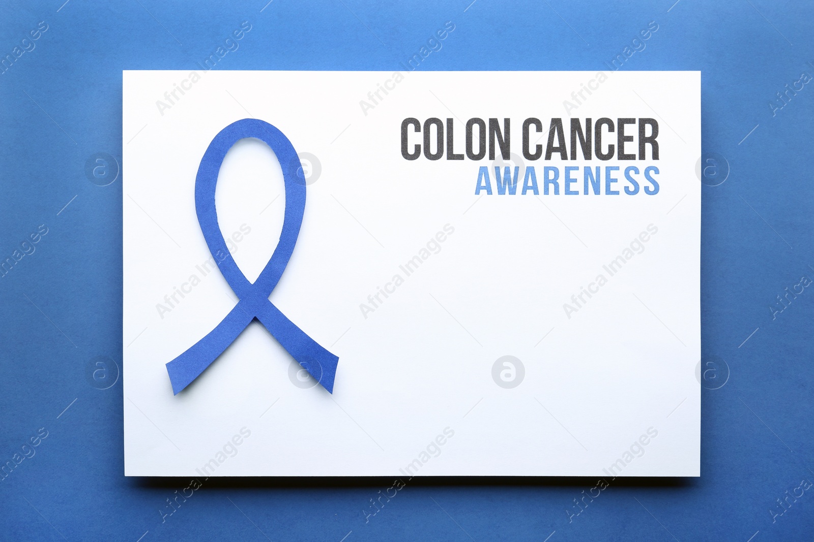 Photo of Card with words COLON CANCER AWARENESS and blue ribbon on color background, top view. Space for text